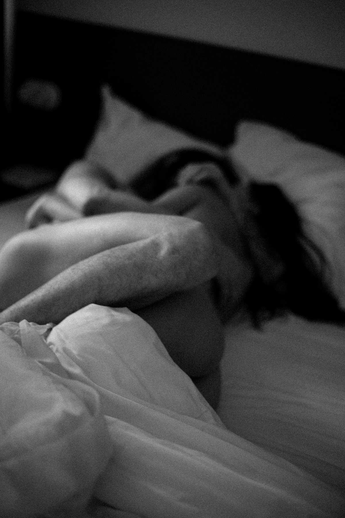A couple embracing on a bed beside a tall window in soft morning light